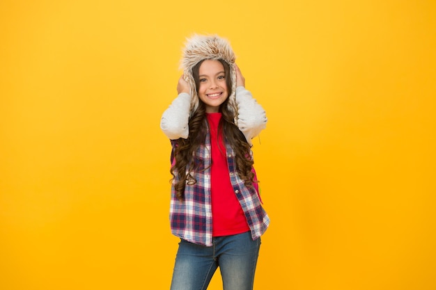 Add some personality to cold weather wardrobe Happy child wear faux fur hat Little girl smile in hat yellow background Fluffy and warm trapper hat for kid Fashion hat for outdoor adventures