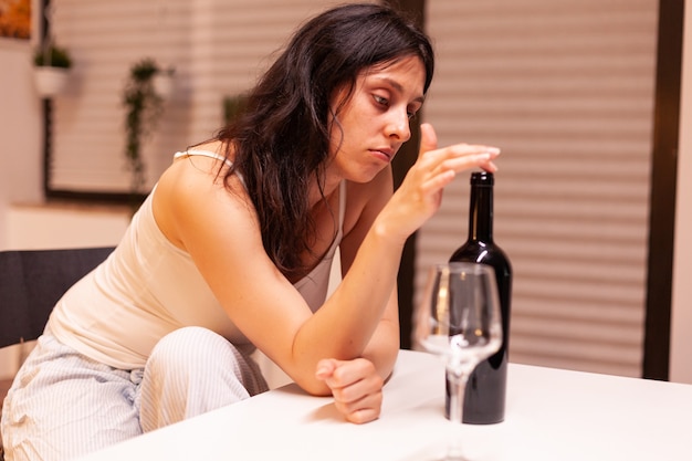 Addicted woman drinking alone at home. Unhappy person suffering of migraine, depression, disease and anxiety feeling exhausted with dizziness symptoms having alcoholism problems.