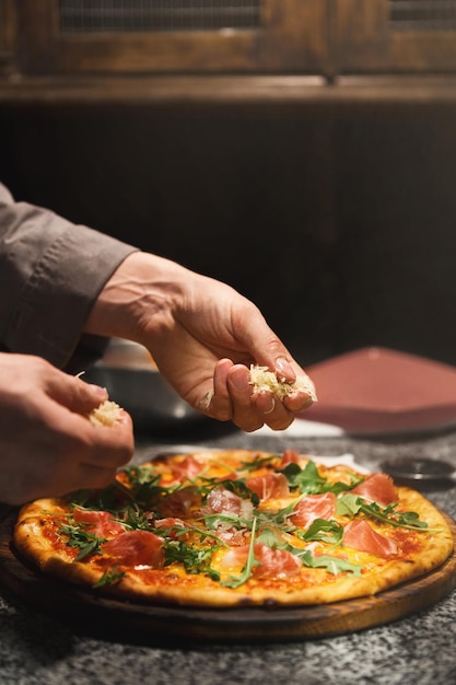 Adding rocket salad to pizza, closeup. Chef put filling on cheese pizza base, copy space