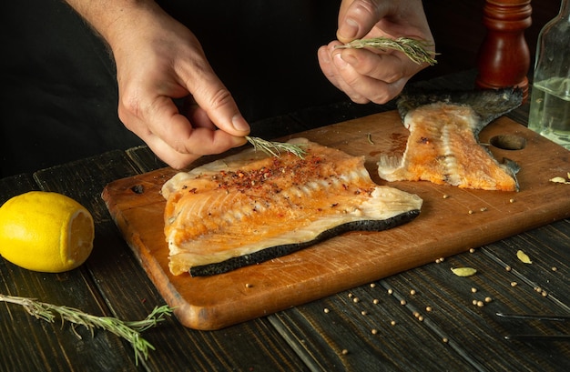 Adding rosemary to fish steaks for aroma and taste Asian cuisine The process of preparing fish by the hands of a chef in a restaurant kitchen