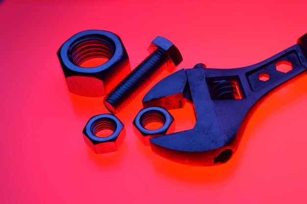 Adjustable wrench and nuts of different sizes on a red backgroundCloseup