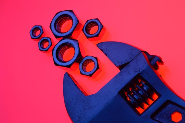 Adjustable wrench and nuts of different sizes on a red backgroundCloseup