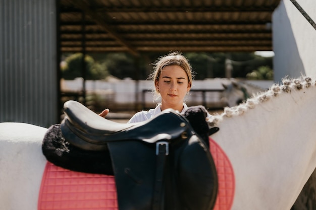 Adolescent placing a saddle on a white horse