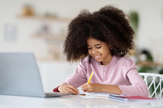 Adorable african american kid doing homework using notebook