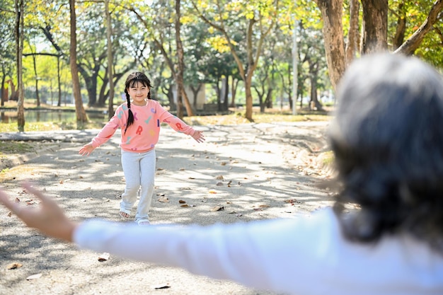 An adorable Asian little girl granddaughter running to her grandmother in the park