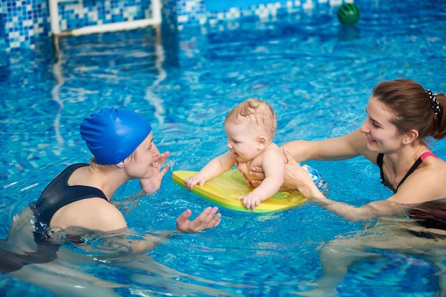 Adorable baby enjoying swimming in pool with mother and trainer helping Side view Newborn baby at sports active family