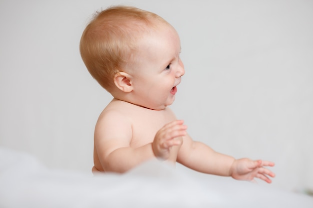 Adorable baby girl in white sunny bedroom. Newborn child relaxing in bed.