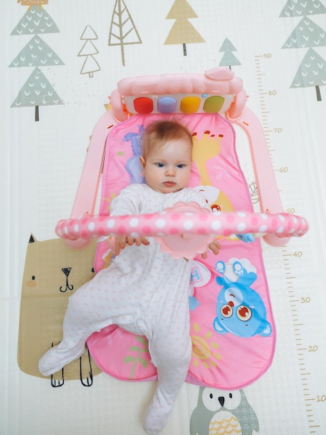 Adorable baby toddler lying on a colorful children's play mat with toys Space for early development and activity of the child baby 6 months