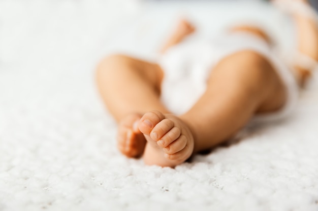 Adorable baby with tiny legs laying on a bed, little toes on a white blanket