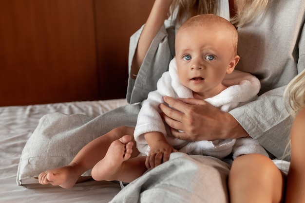 Adorable blue-eyed baby boy in a white robe with a hood sitting in his mother's arms