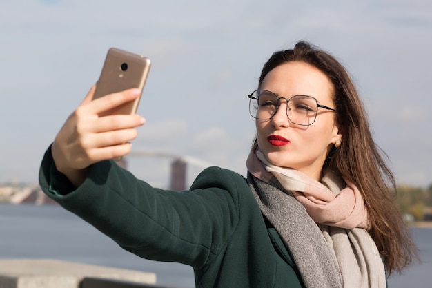 Adorable brunette woman tourist taking a selfie photo on a coast of river in Kyiv