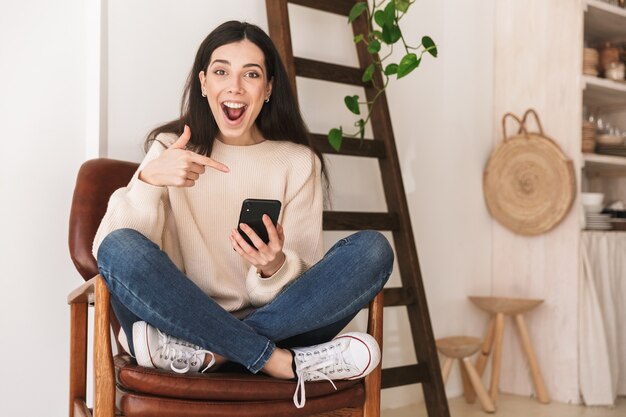 adorable cauasian woman resting in apartment and using cell phone while sitting on chair