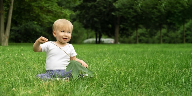 Adorable caucasian baby girl sitting on grass in park in summer infant playingcopyspace