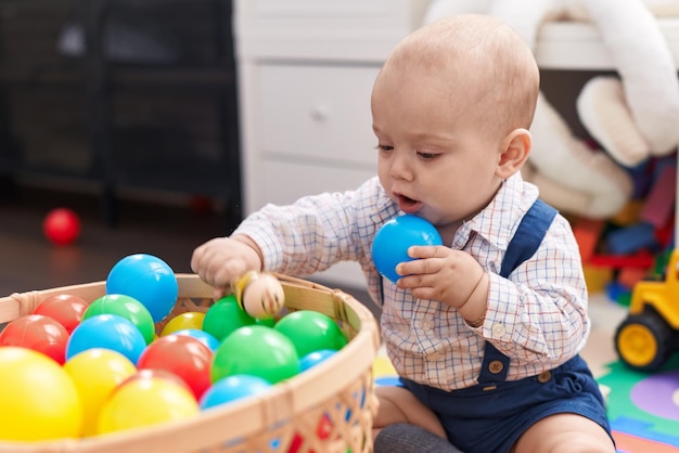 Adorable caucasian baby playing with balls sitting on floor at kindergarten