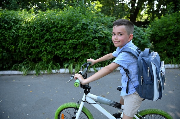 Adorable child boy with school bag , riding a bicycle cute smiles looking at camera. Back to school concept