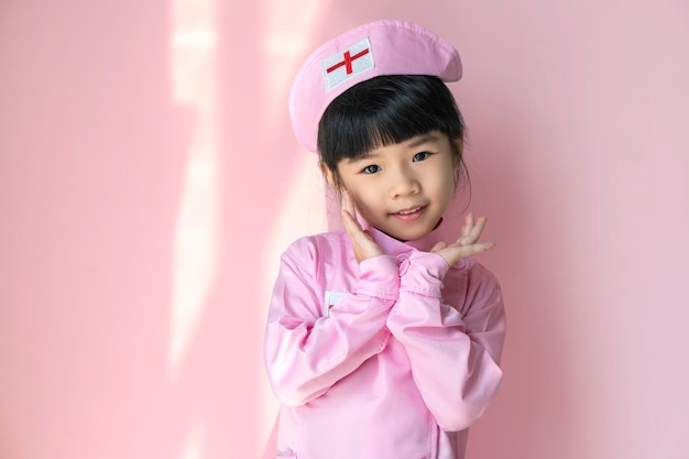 Adorable child girl uniformed as doctor isolated on pink background