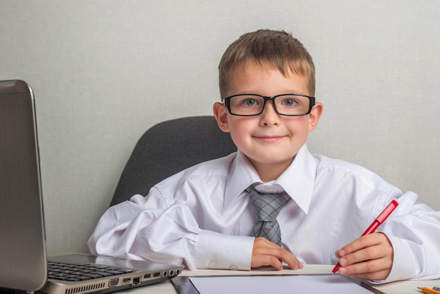 An adorable child is working on a laptop in suit and glasses