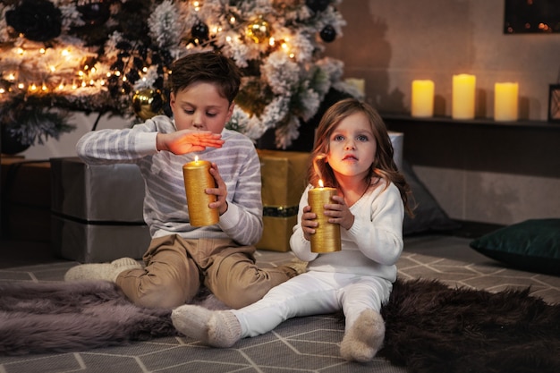 Adorable children boy and girl holding yellow candles and making wish Christmas tree and presents