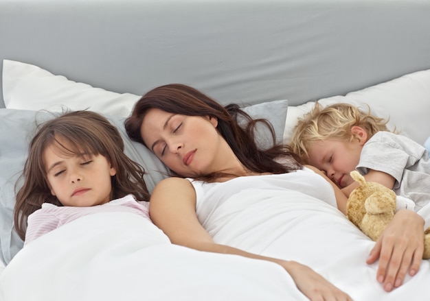 Adorable children sleeping with their mother on her bed