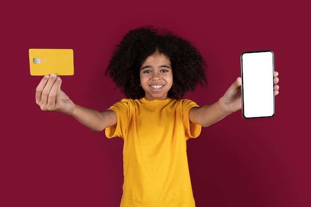 Adorable curly black girl showing cell phone and credit card