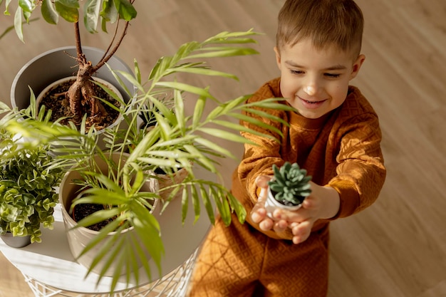 Adorable cute boy caring of indoor plants at home A little helper in the household leisure activity Home gardening concept Cozy room earth colors Casual clothing