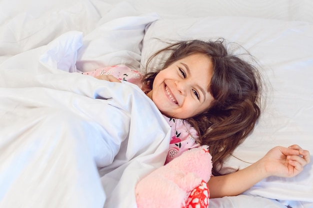 Adorable dark hair girl sleeping sweetly in the morning on wihte bed linens at home Childrens dreams comfort rest and peace