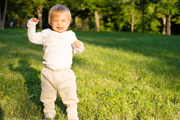 Adorable funny caucasian blonde baby girl laughing standing on grass in park outdoors, Copy space for text.