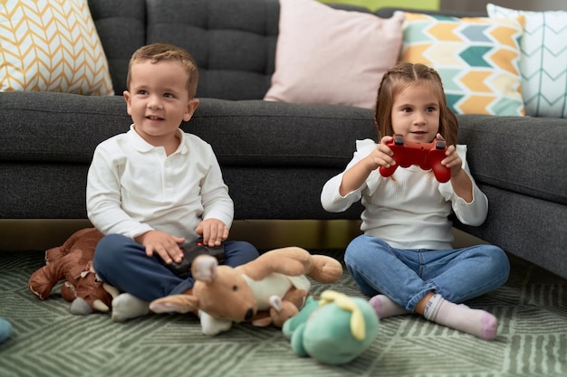 Adorable girl and boy playing video game sitting on floor at home