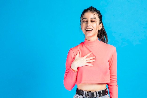 Adorable girl close her eyes and put her hand to her chest on blue background High quality photo