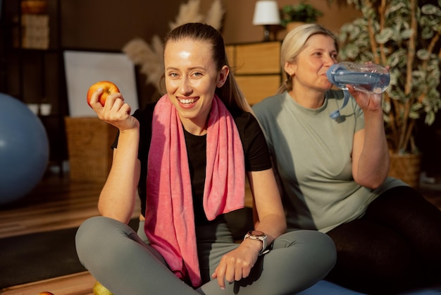 Adorable girl looking at camera holding ripe apple in arm relaxing with elderly woman in background