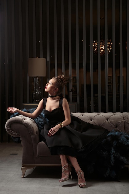 Adorable girl sitting in dark elegant room and looking aside