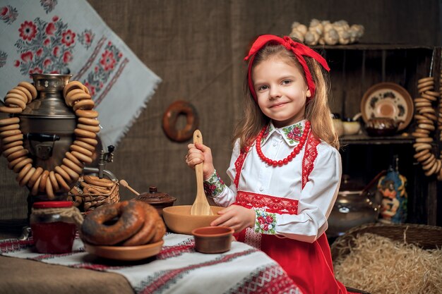 Adorable girl sitting at table full of food and big samovar. Traditional celebrating Maslenitsa