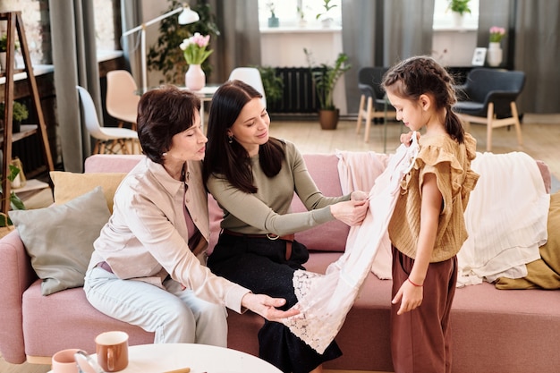 Adorable girl trying on new dress in front of her mother and grandmother