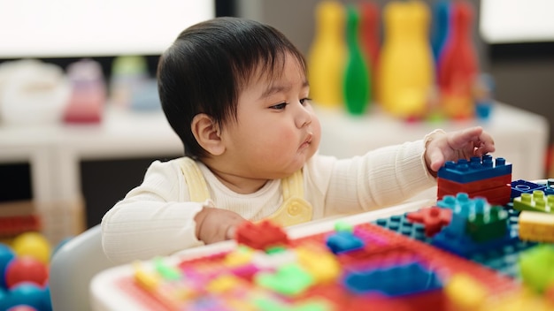 Adorable hispanic baby playing with construction blocks sitting on table at kindergarten