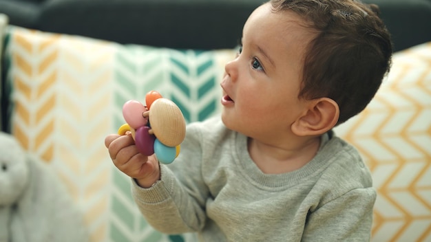 Adorable hispanic baby sucking pacifier sitting on bed at home