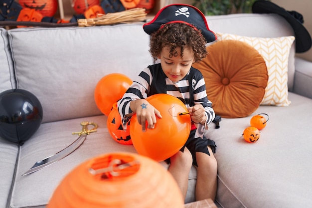 Adorable hispanic boy having halloween party drawing on balloon at home