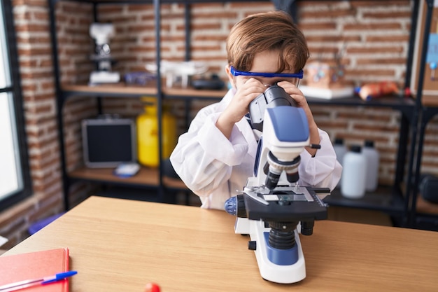 Adorable hispanic boy student using microscope at laboratory classroom