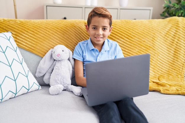 Adorable hispanic boy using laptop sitting on sofa at home