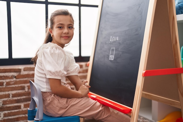 Adorable hispanic girl student smiling confident drawing on blackboard at classroom