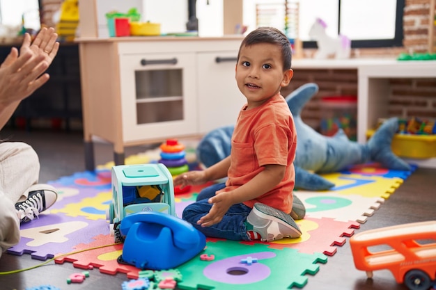 Adorable hispanic toddler smiling confident sitting on floor playing at kindergarten