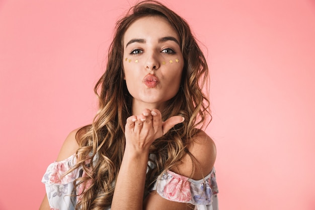 adorable lady wearing dress blowing air kiss to you, isolated on pink