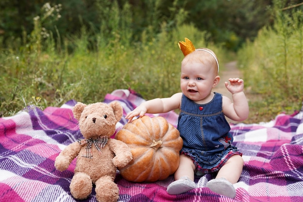 Adorable little baby girl having fun with pumpkin and toy teddy bear on beautiful autumn day outdoors. Happy child playing in autumn park