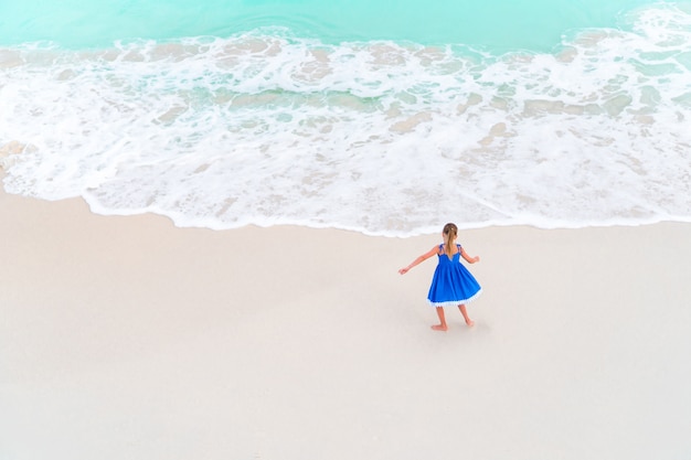 Adorable little girl dancing on white tropical beach. View from above of a deserted beach with turquoise water