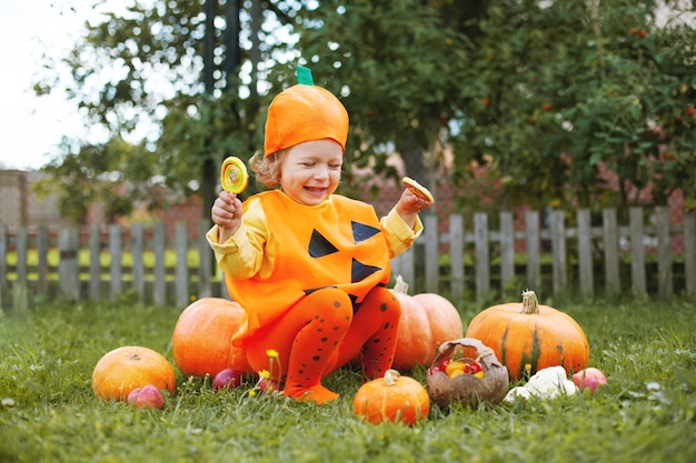 Photo adorable little girl in halloween themed clothing sitting on a large orange pumpkin