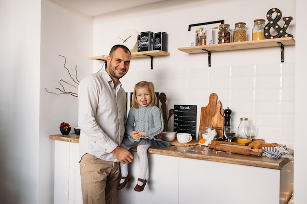 Adorable little girl is sitting on kitchen table with father. 