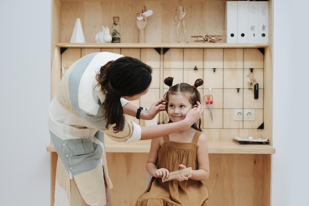 Adorable little girl is sitting on stool patiently enduring mom doing her hair