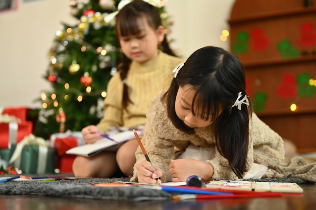 Adorable little girl making greeting card for New Year and Christmas while lying on carpet