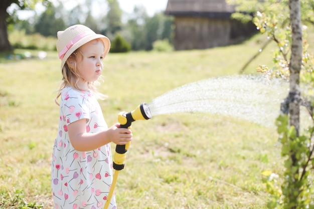 Adorable little girl playing with a garden hose on hot and sunny summer day