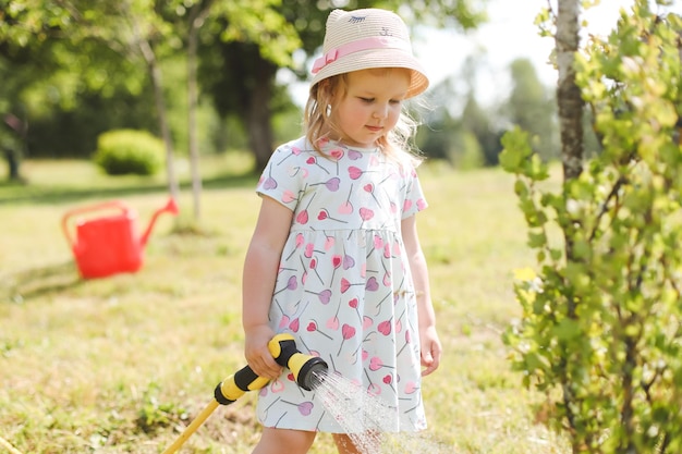 Adorable little girl playing with a garden hose on hot and sunny summer day