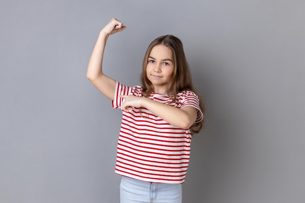 Photo adorable little girl raising hand pointing biceps feeling power and energy to achieve goal